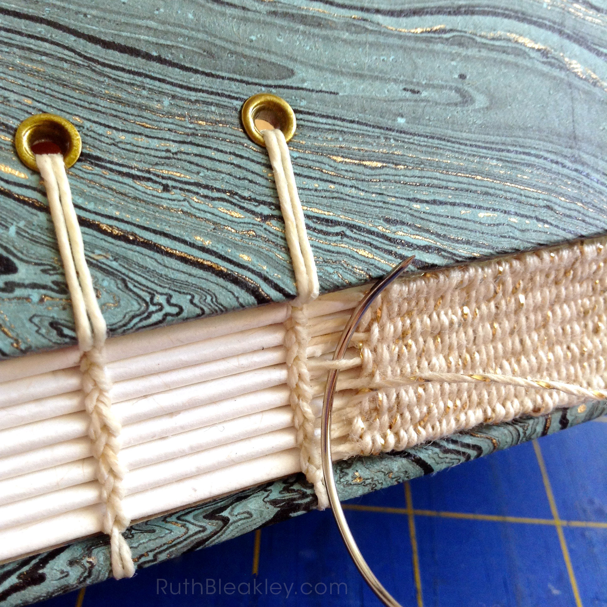 Woven spine on a handmade book using gold and white thread.